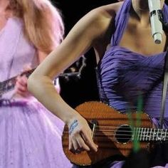 a woman in a purple dress holding a guitar and singing into a microphone while another woman stands behind her