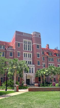 an old brick building with palm trees in the foreground and green grass on the ground