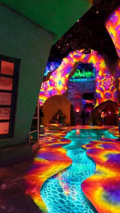 an indoor art installation with colorful lights and water running through the floor, in front of a large archway