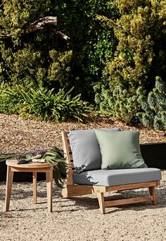 a chair and table sitting in the middle of a graveled area with bushes behind it