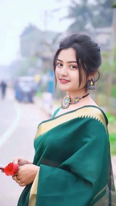 a woman in a green and yellow sari holding a red flower on the street