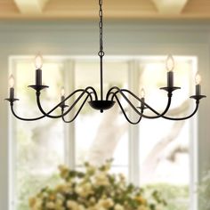 a chandelier hanging from the ceiling in a dining room with flowers on the table