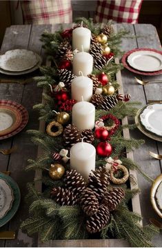 a wooden table topped with lots of candles and pine cones covered in christmas decorations on top of it