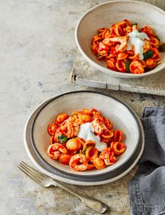 two bowls filled with pasta and sauce on top of a table next to silverware