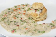 a white plate topped with chicken pot pie next to a biscuit covered in gravy