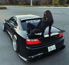 a woman sitting on the hood of a black sports car