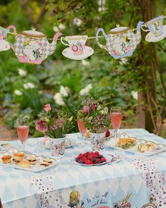 a table topped with tea cups and plates filled with food next to flowers in vases