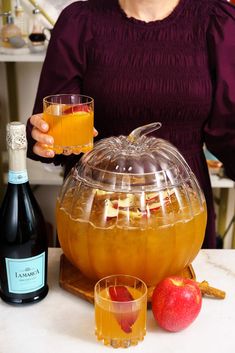 a woman holding a glass in front of an apple cider and two wine glasses