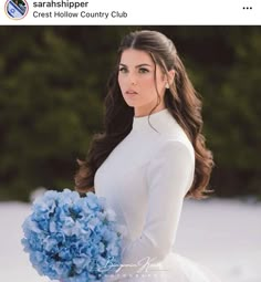 a woman in a white dress holding a bouquet of blue hydrangeas and looking at the camera