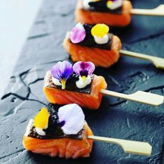 four sushi with flowers on them sitting on top of a black slate countertop