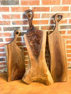 three wooden cutting boards sitting next to each other on top of a wood floor in front of a brick wall