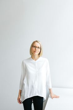 a woman standing in front of a white wall with her hands on her hips and looking at the camera