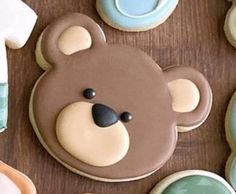 decorated cookies with teddy bears and baby ones on top of a wooden table next to cupcakes in the shape of t - shirts