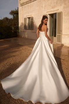 a woman in a white wedding dress standing on the side of a building with her back to the camera