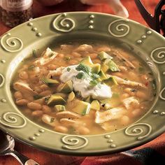 a bowl of chicken and bean soup with sour cream on the table next to it