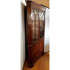 a tall wooden cabinet with glass doors on the top and bottom, against a white wall