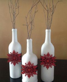 three white bottles with branches in them on a table