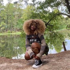 a woman sitting on the ground next to a lake with trees in front of her