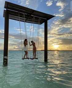 two women on swings in the ocean at sunset