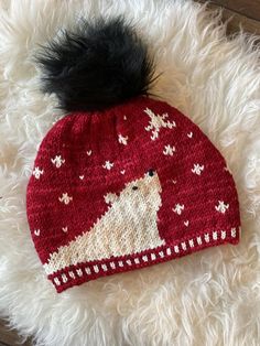 a knitted hat with a pom - pom sits on top of a fluffy white rug