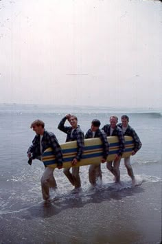 four men carrying their surfboards into the water at the beach while wearing flannel