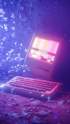 an old computer sitting on top of a wooden table in front of purple and red flowers