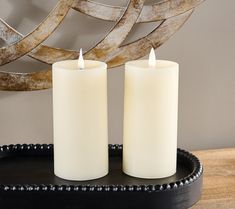 two white candles sitting on top of a black tray