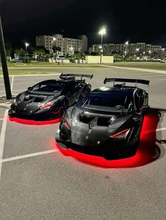 two black and red sports cars parked next to each other in a parking lot at night