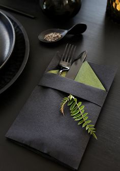 a place setting with silverware and green napkins on a black table cloth,