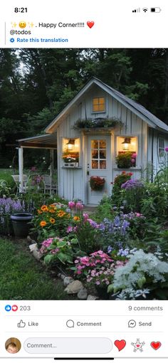 a small white shed with flowers in the front yard and lights on it's windows