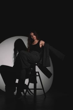 a woman sitting on top of a stool in front of a white ball and black background