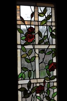 a stained glass window with red flowers and green leaves on the outside, against a dark background