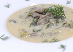 a white plate topped with soup and meat covered in gravy, garnished with green herbs