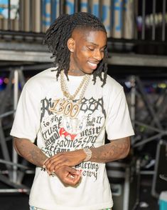 a young man with dreadlocks standing in front of a microphone and looking at his cell phone