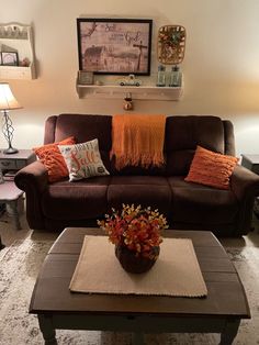 a living room with brown couches and orange pillows on the coffee table in front of it