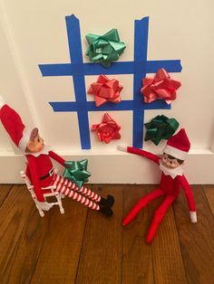 two elfs are sitting on the floor next to a wall with presents wrapped in red and green paper