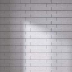 an empty room with white brick walls and a floor lamp in the corner, casting a shadow on the wall