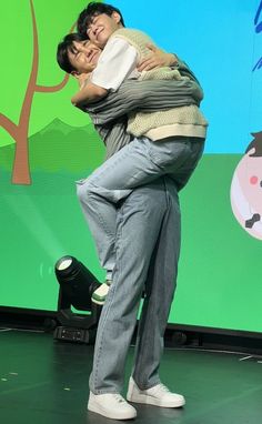 a man and woman hug each other while standing on stage with a green screen behind them