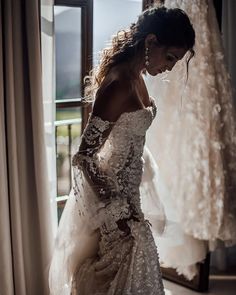 a woman standing in front of a window wearing a wedding dress