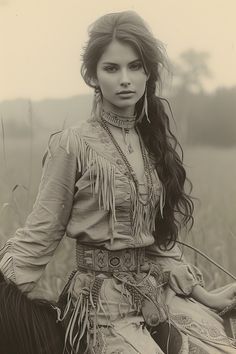 an old photo of a woman in native clothing on a horse with grass behind her