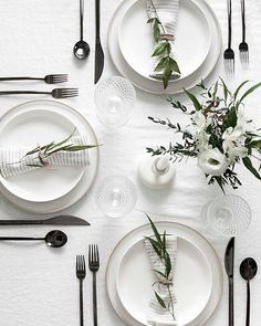 the table is set with black and white plates, silverware, and flower centerpieces