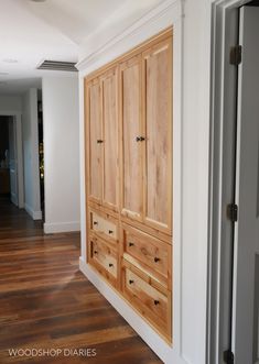 an empty room with white walls and wooden cabinets in the center, along with hard wood flooring