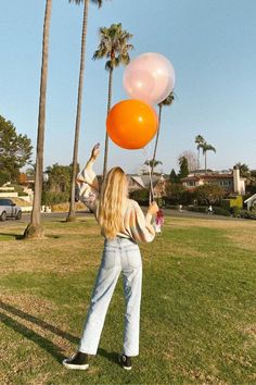 a woman holding two orange and white balloons in her hand while standing on the grass