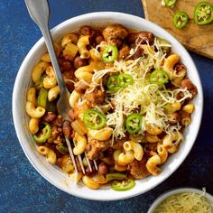 a white bowl filled with pasta and meat covered in cheese, green peppers, and parmesan cheese