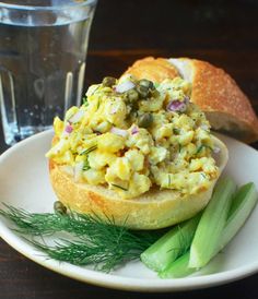 there is a sandwich with eggs and vegetables on the plate next to a glass of water