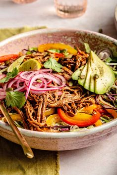 a bowl filled with meat, vegetables and avocado on top of a table