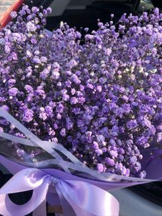 a bouquet of purple flowers in front of a car with a ribbon tied around it