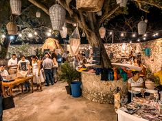 a group of people standing around tables with food on them and hanging from the ceiling