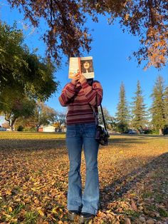 a woman standing under a tree while holding up a book in front of her face