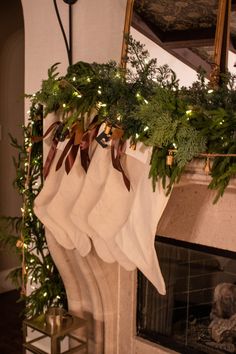 stockings hanging from a fireplace with christmas lights and greenery on the mantel above them